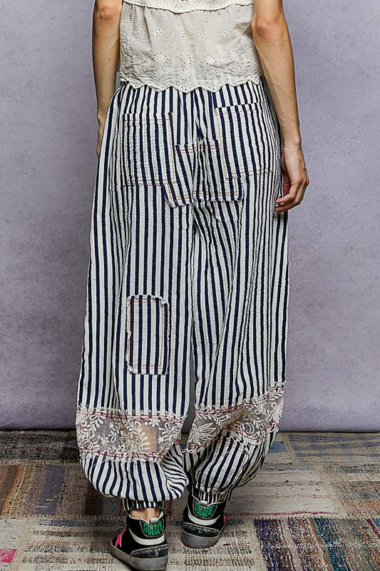 Person wearing black and white striped pants with a patterned hem on a plain background