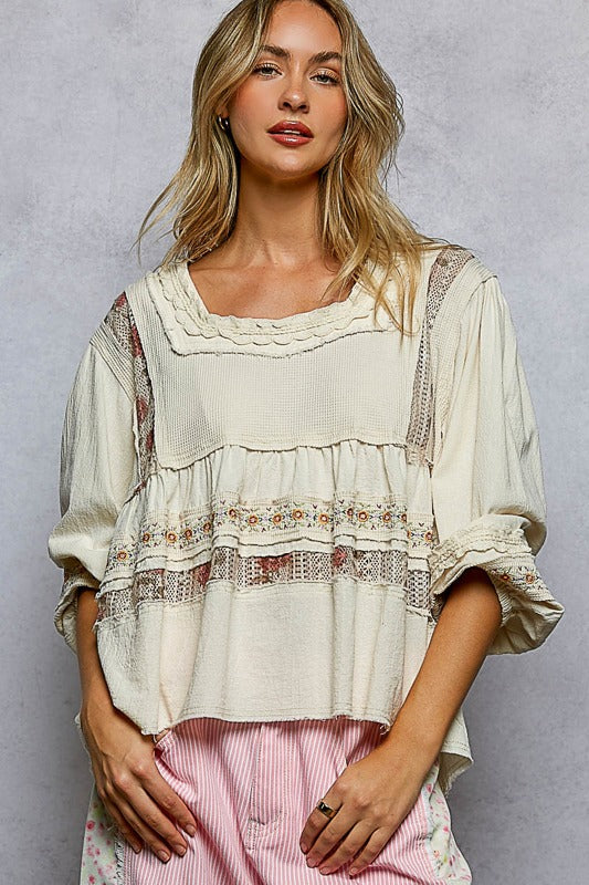 Woman wearing a white blouse with lace details against a gray background