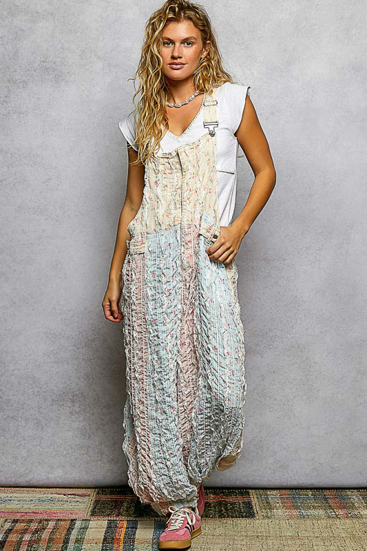 Woman wearing a long, patterned overall over a white shirt against a gray background