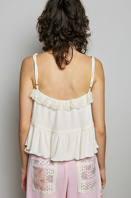 Woman wearing a white lace top and pink pants with lace details on a plain background