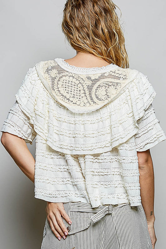 Woman wearing a textured white top with a patterned back on a plain background