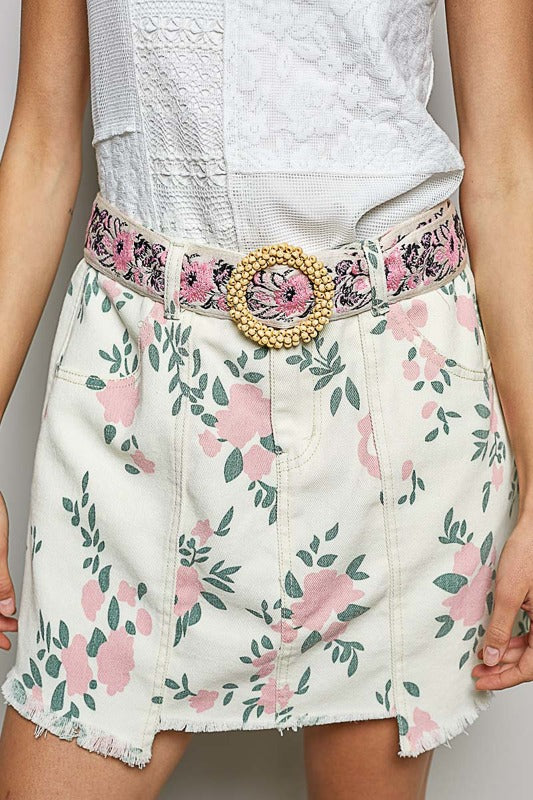 Person wearing a floral skirt with a decorative belt on a plain background
