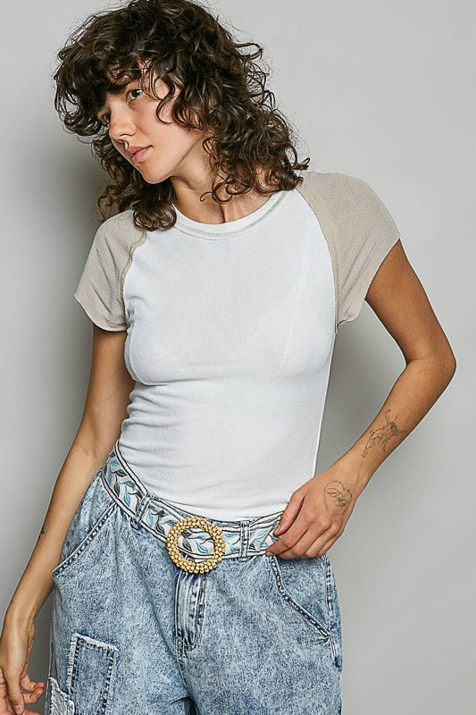 Person wearing a white and beige baseball shirt with blue jeans against a plain background