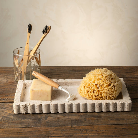 Set of bamboo toothbrushes, glass, soap, and sponge on a stone tray with a wooden background.