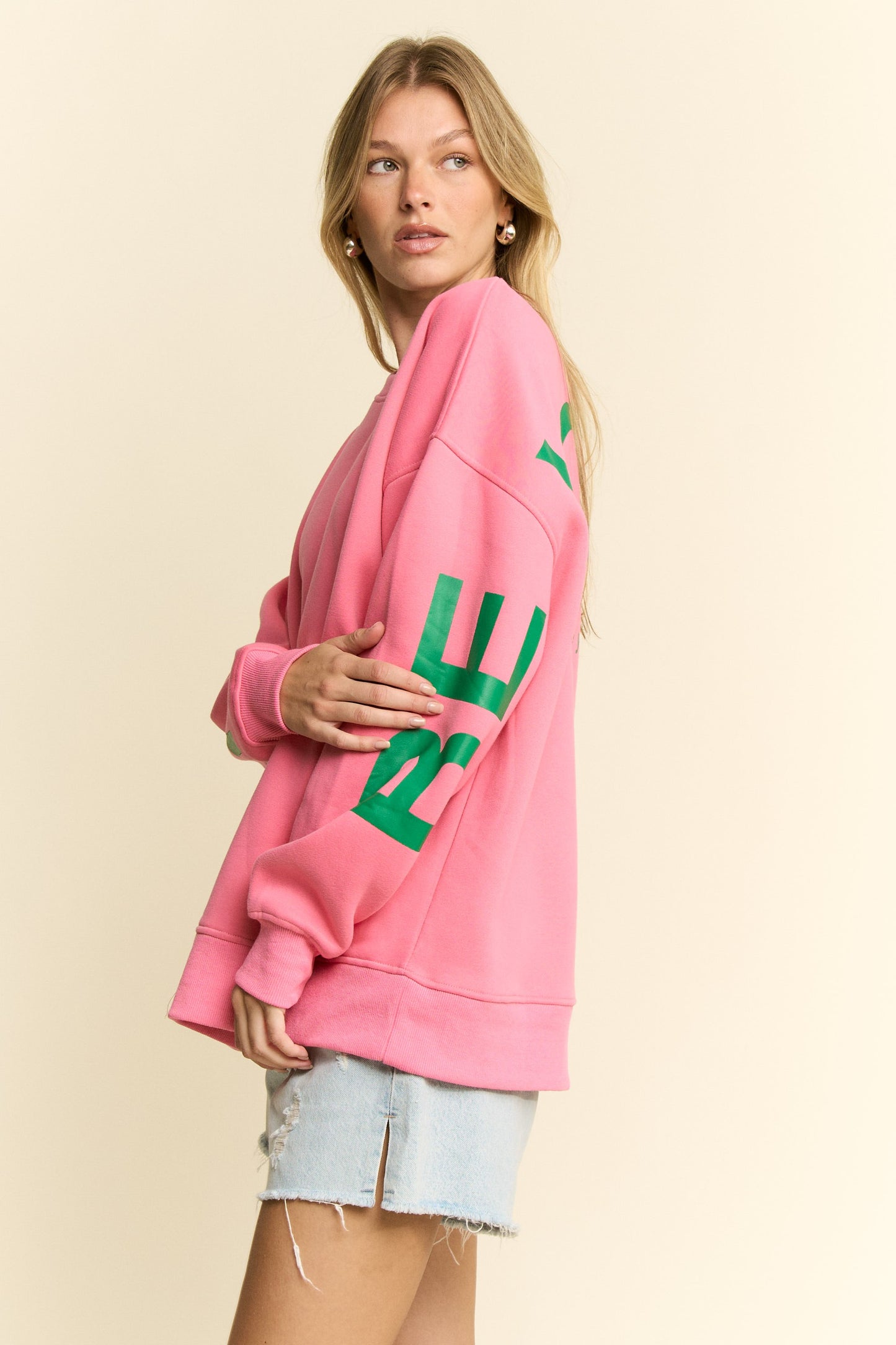 Woman wearing a pink sweatshirt with green text on a beige background