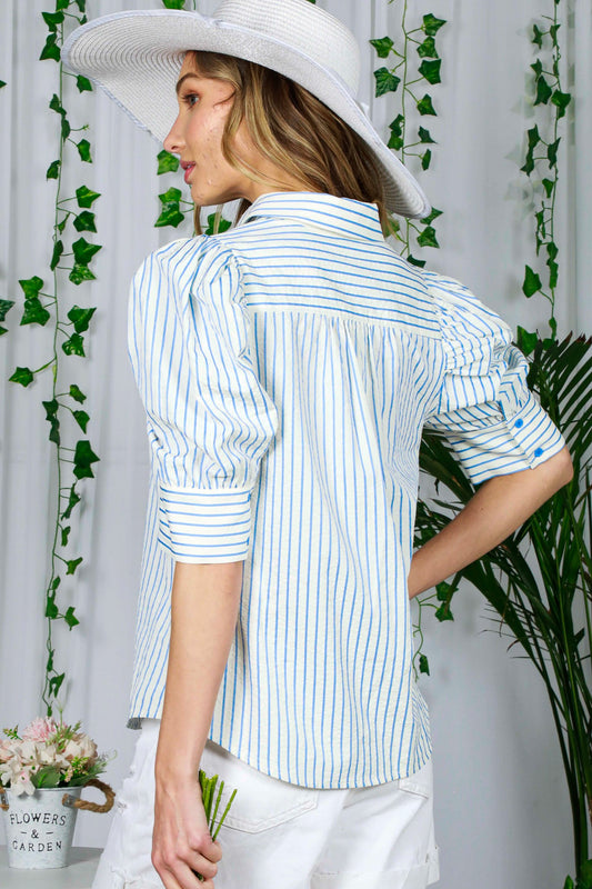 Woman wearing a white and blue striped shirt with a white hat, standing against a white background with greenery.