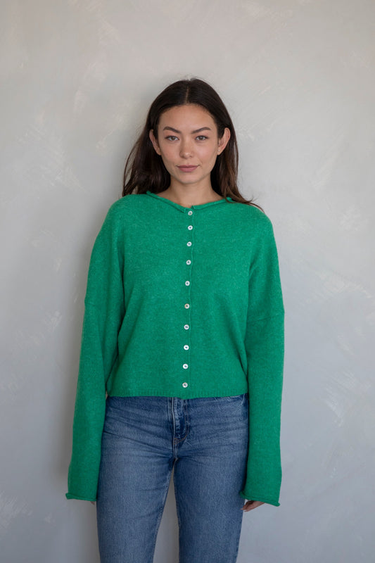Woman wearing a green long-sleeve shirt with buttons and blue jeans against a plain background