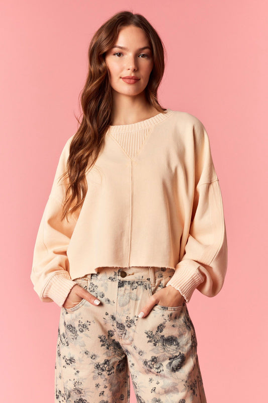 Woman wearing a light orange sweater and floral pants against a pink background