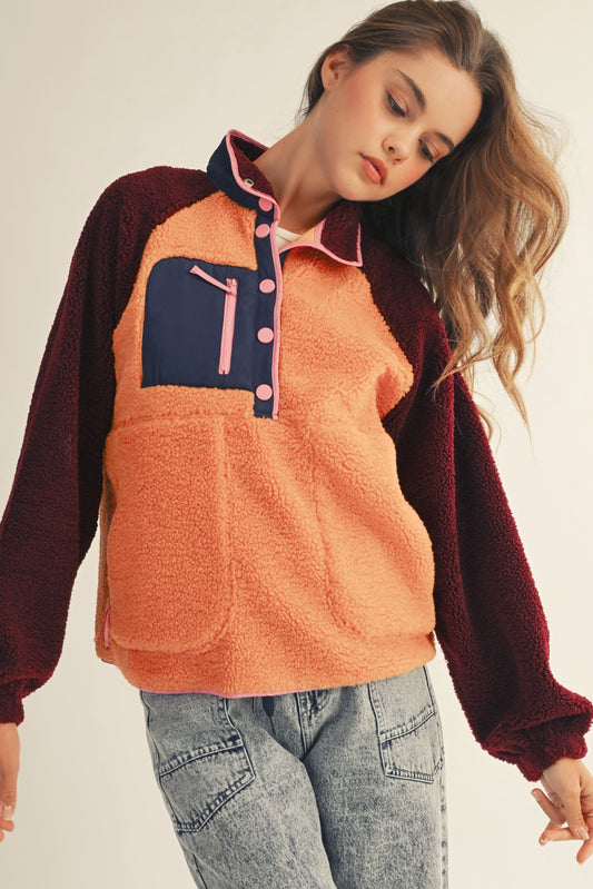 Woman wearing a two-tone pullover with an orange front and maroon sleeves on a plain background