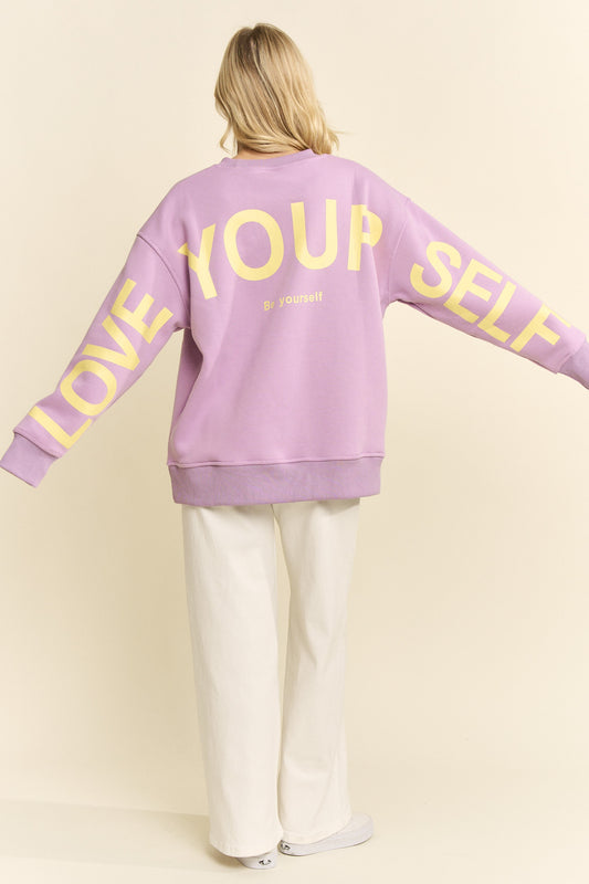 Person wearing a purple sweatshirt with 'Love Your Self' text on a plain background