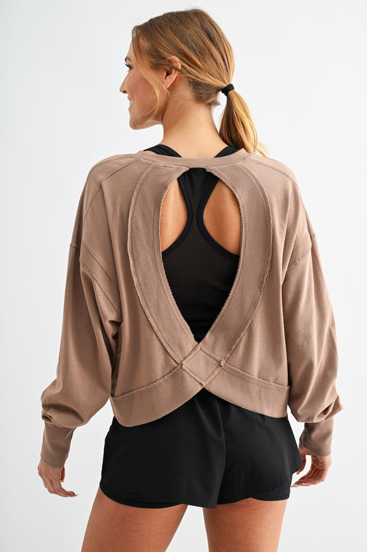 Woman wearing a beige open-back cardigan over a black top and shorts on a white background