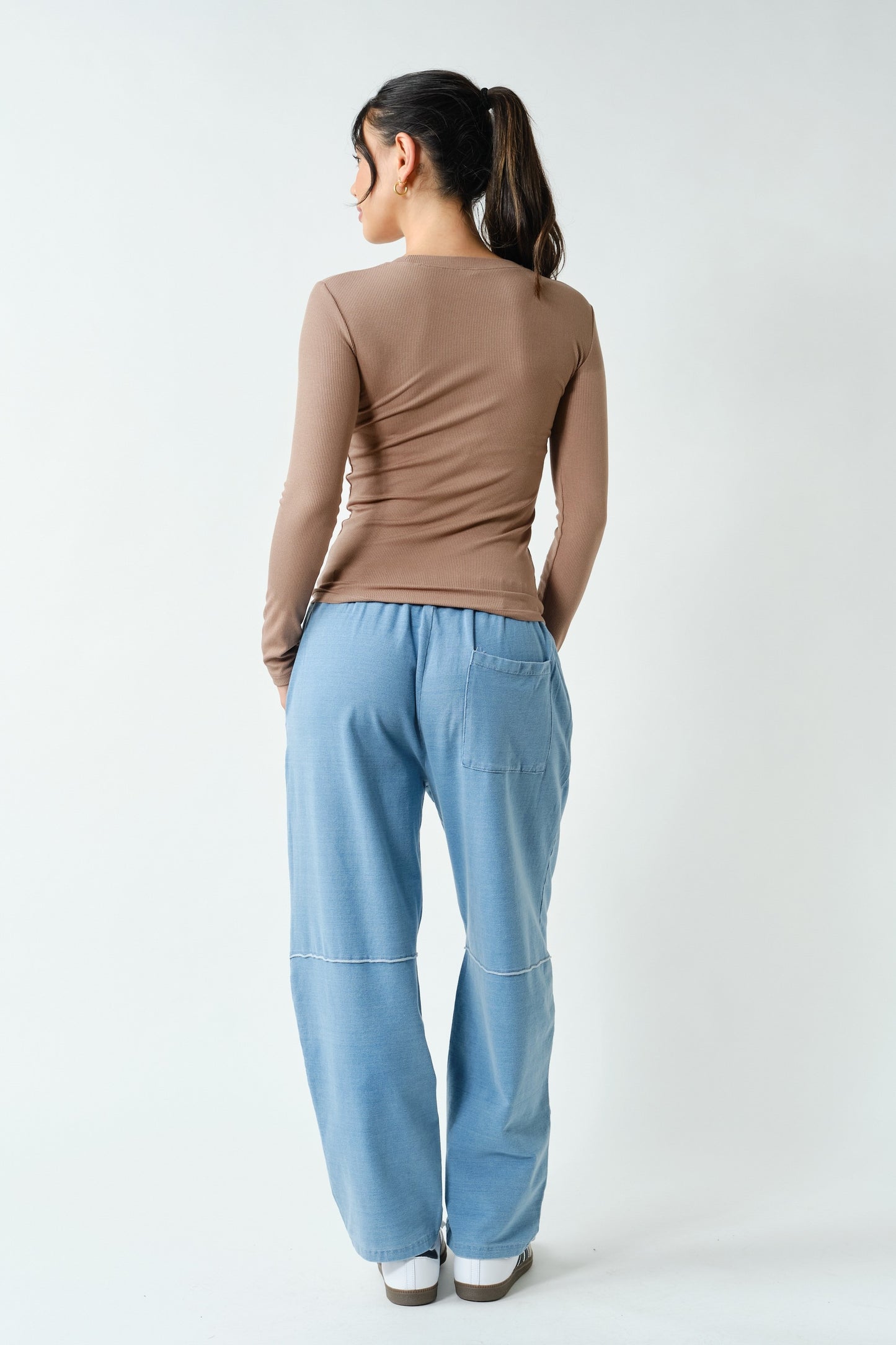 Person wearing a brown top and light blue pants on a white background