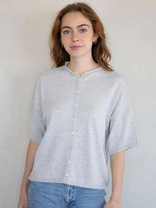 Woman wearing a light gray cardigan over a white shirt with blue jeans against a plain background