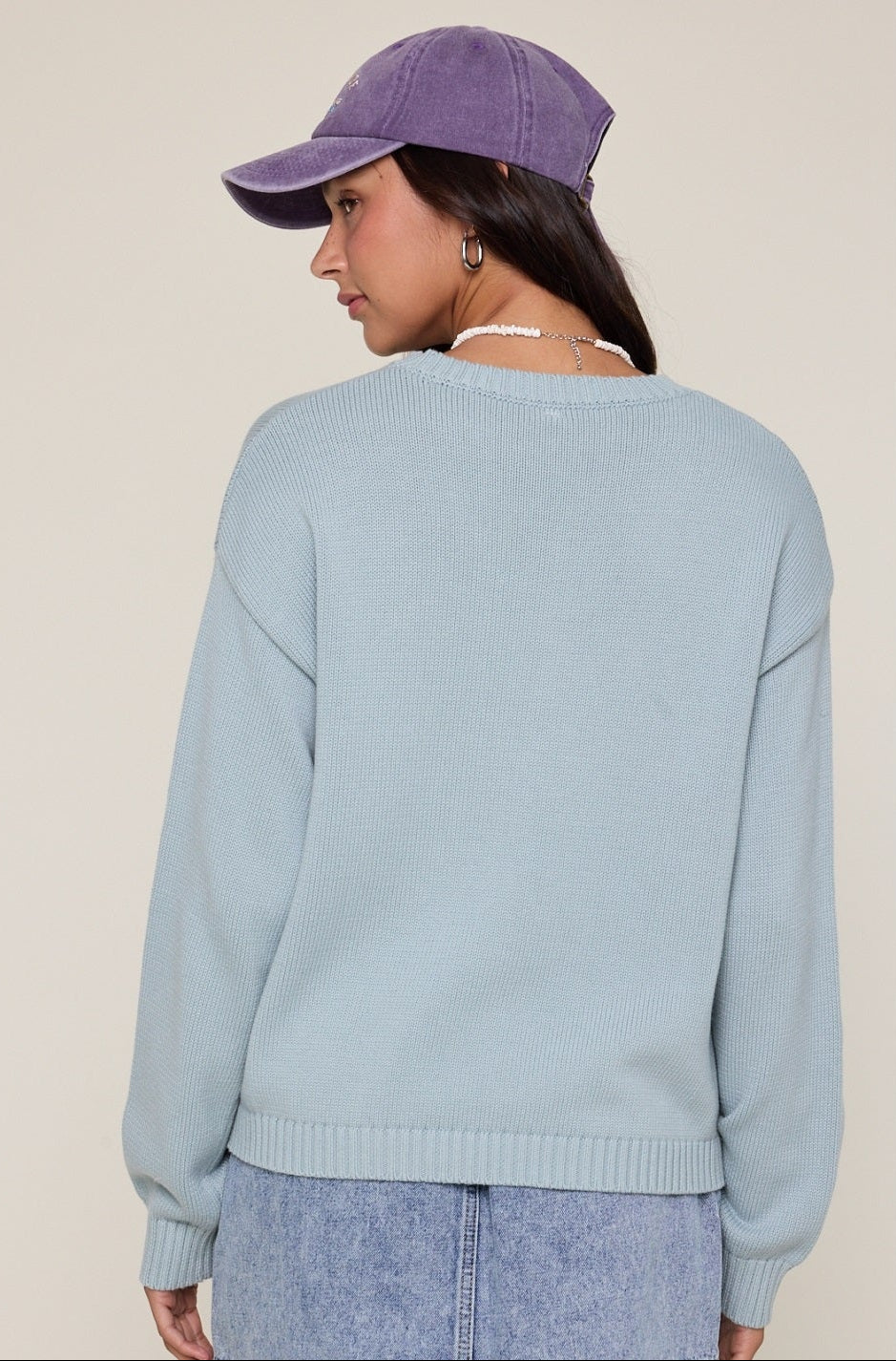 Person wearing a light blue sweater and purple cap on a beige background