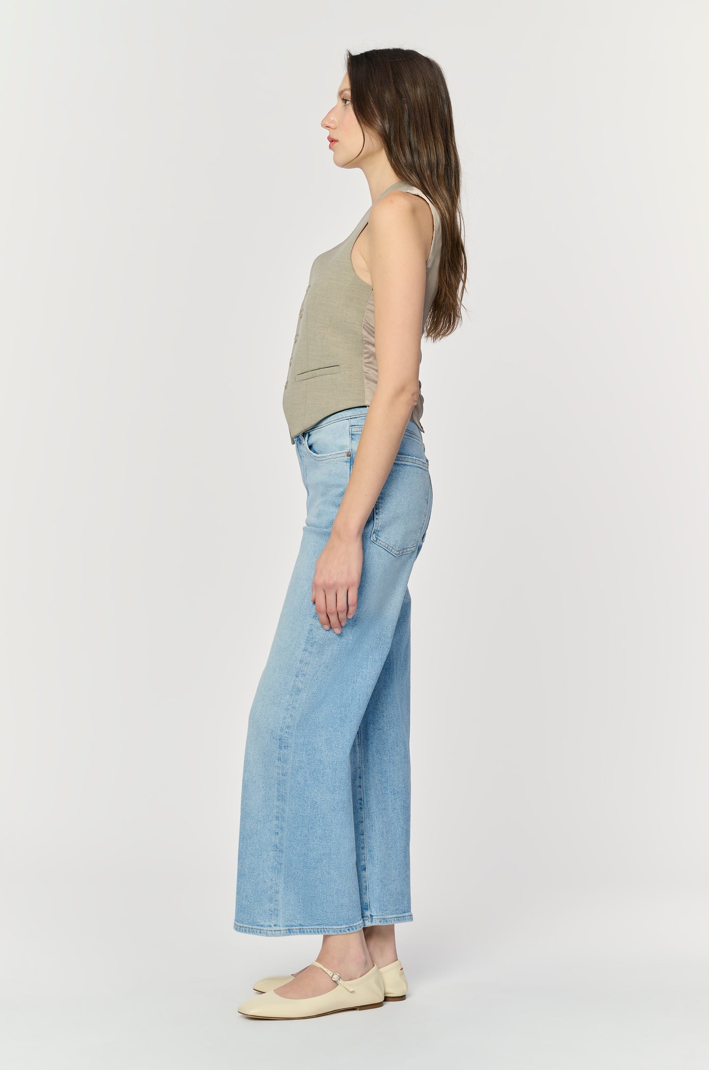 Woman wearing light blue jeans and a beige top on a white background