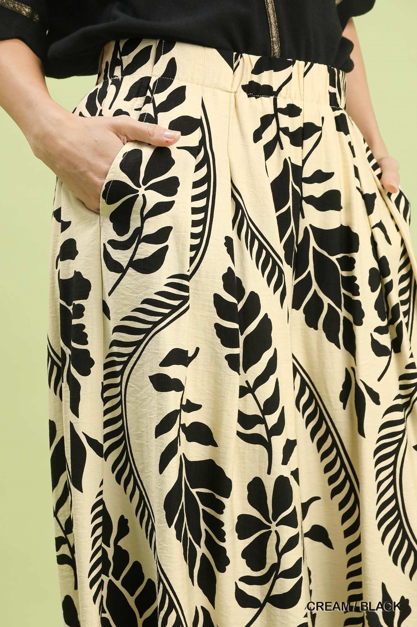 Beige pants with black leaf pattern worn by a person on a light green background