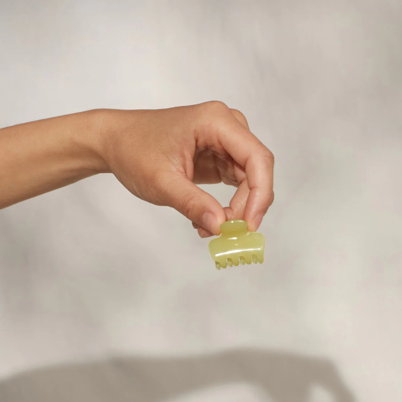 Hand holding a small green hair clip against a plain background