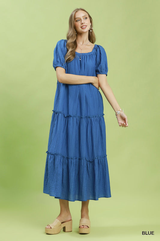 Woman wearing a blue tiered dress on a green background