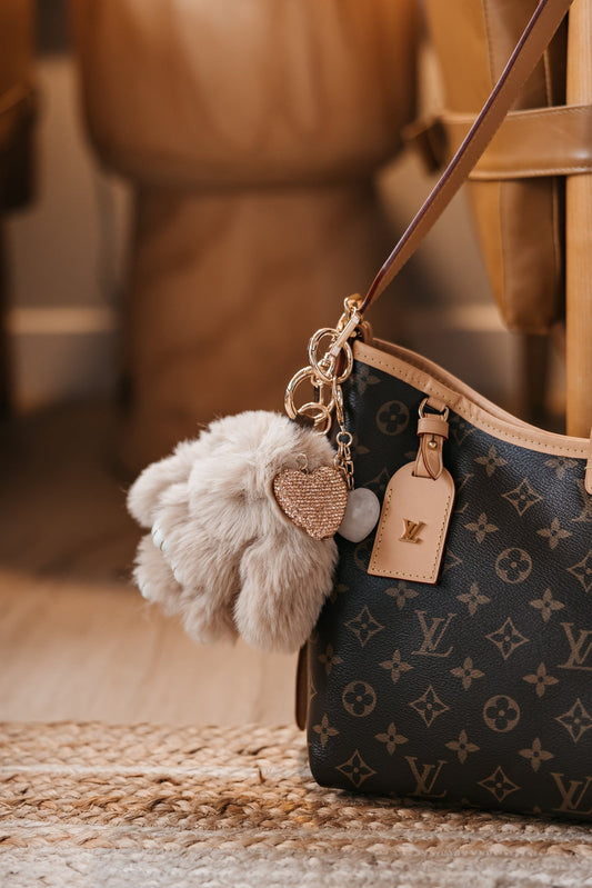 Designer handbag with decorative keychain featuring fluffy pom-pom and heart charm.
