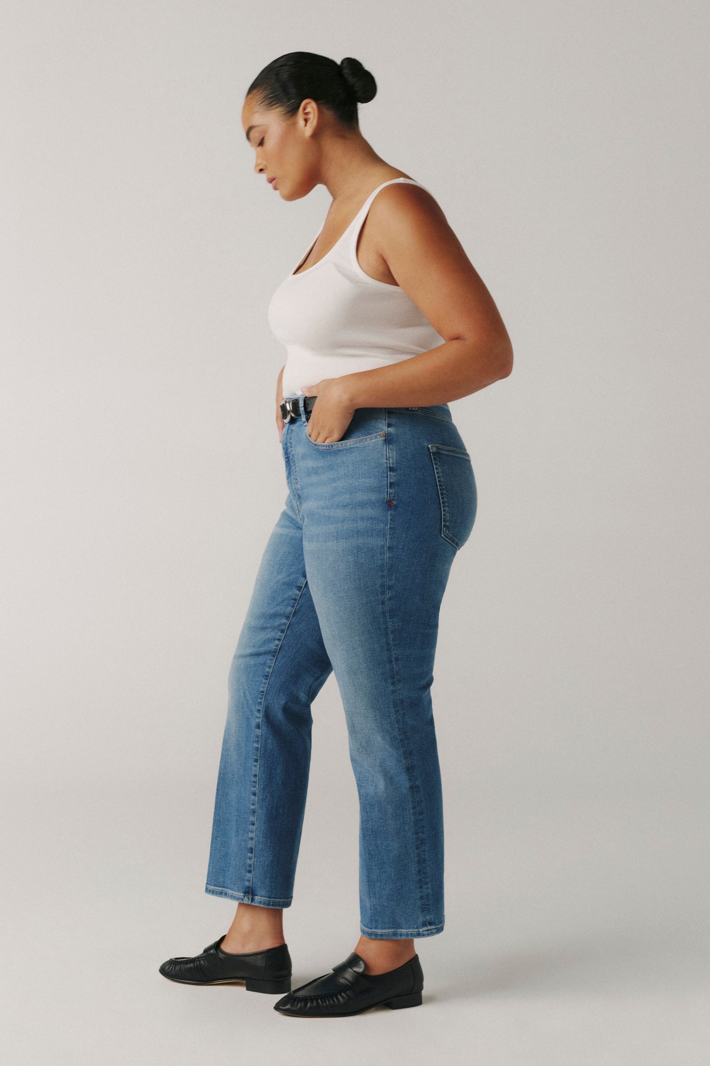 Woman wearing a white tank top and blue jeans on a plain background