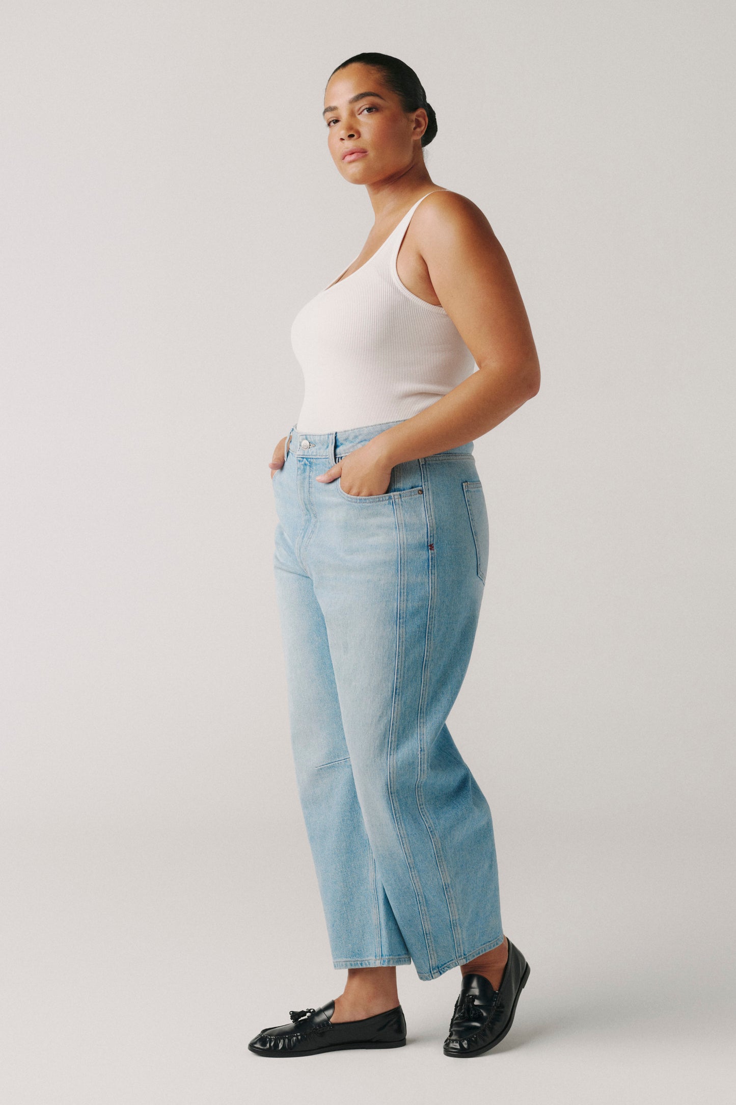 Woman wearing a white tank top and light blue jeans against a plain background