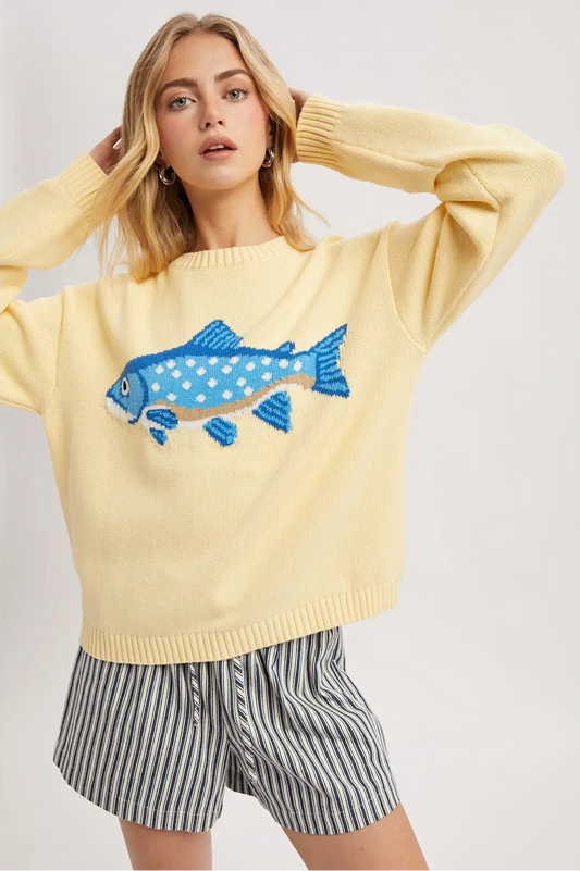Woman wearing a yellow sweater with a blue fish design on a plain background