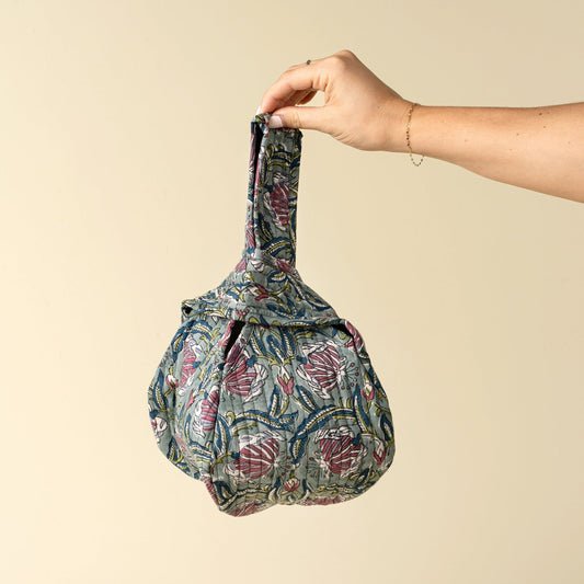 Hand holding a patterned bag against a beige background