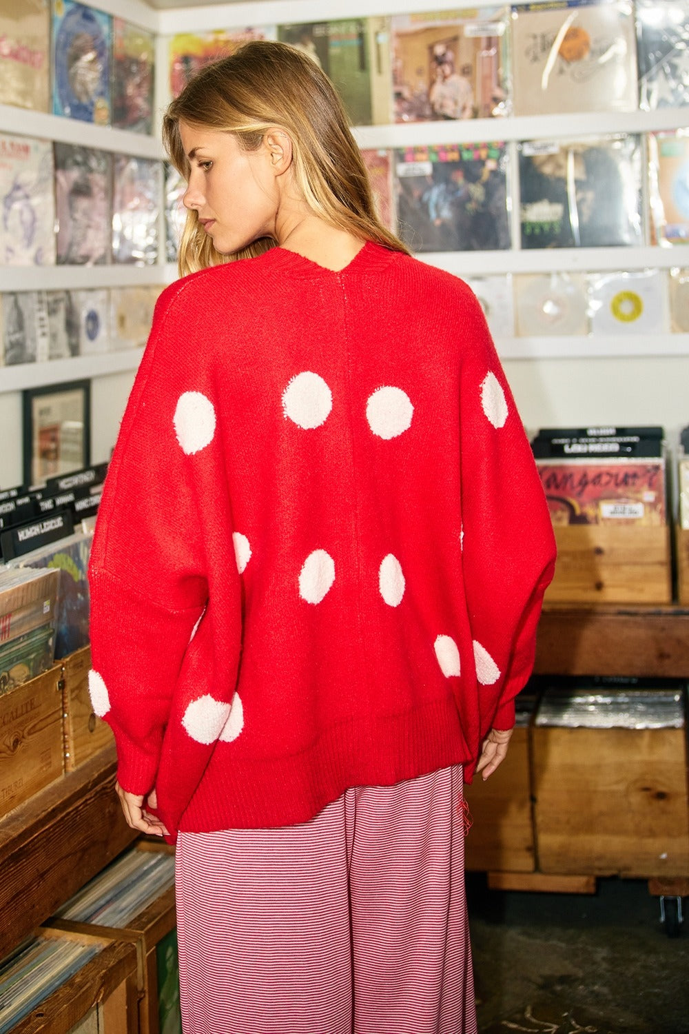 Person wearing a red sweater with white polka dots in a record store.