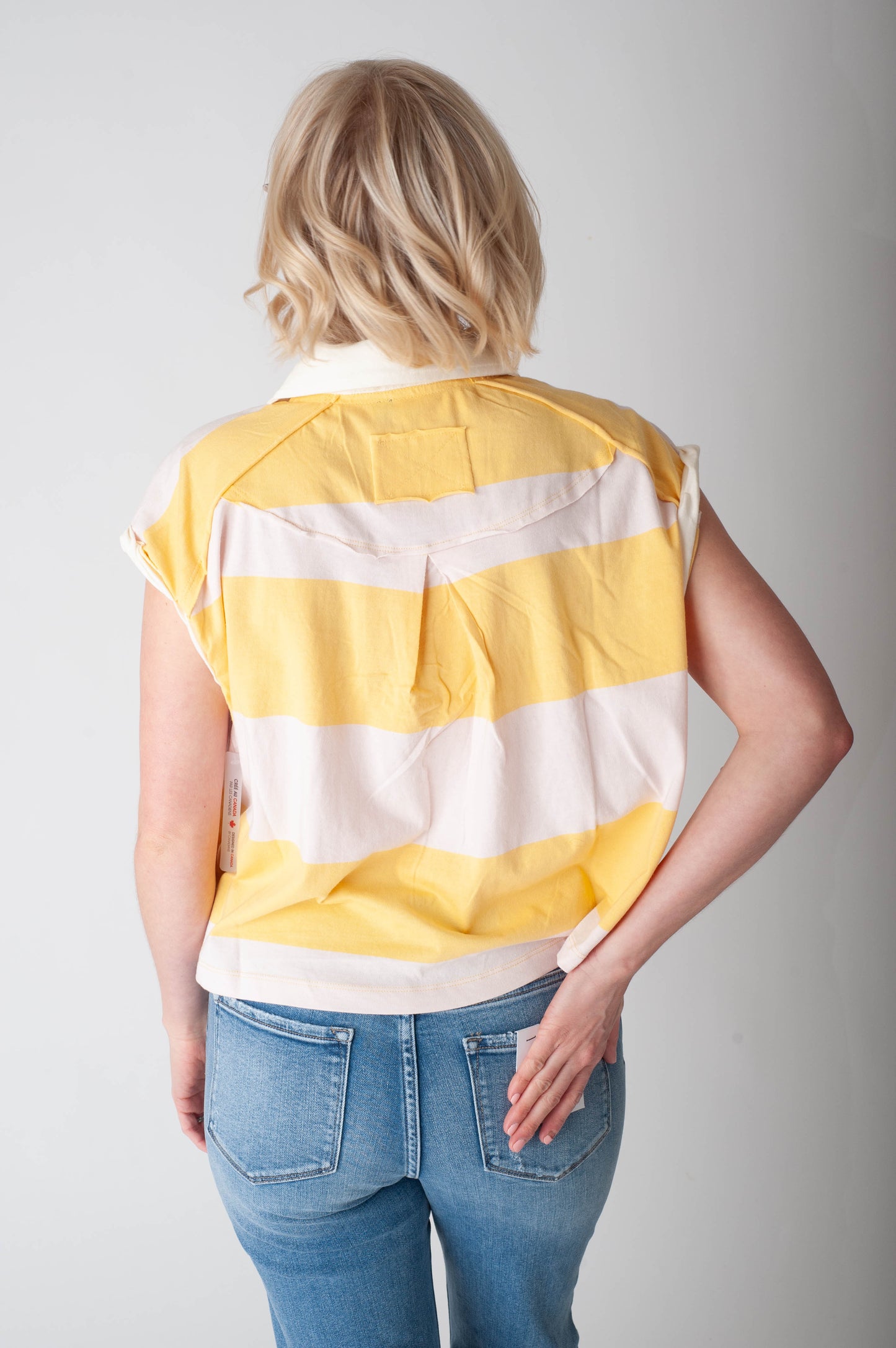 Person wearing a yellow and white striped shirt with blue jeans on a plain background