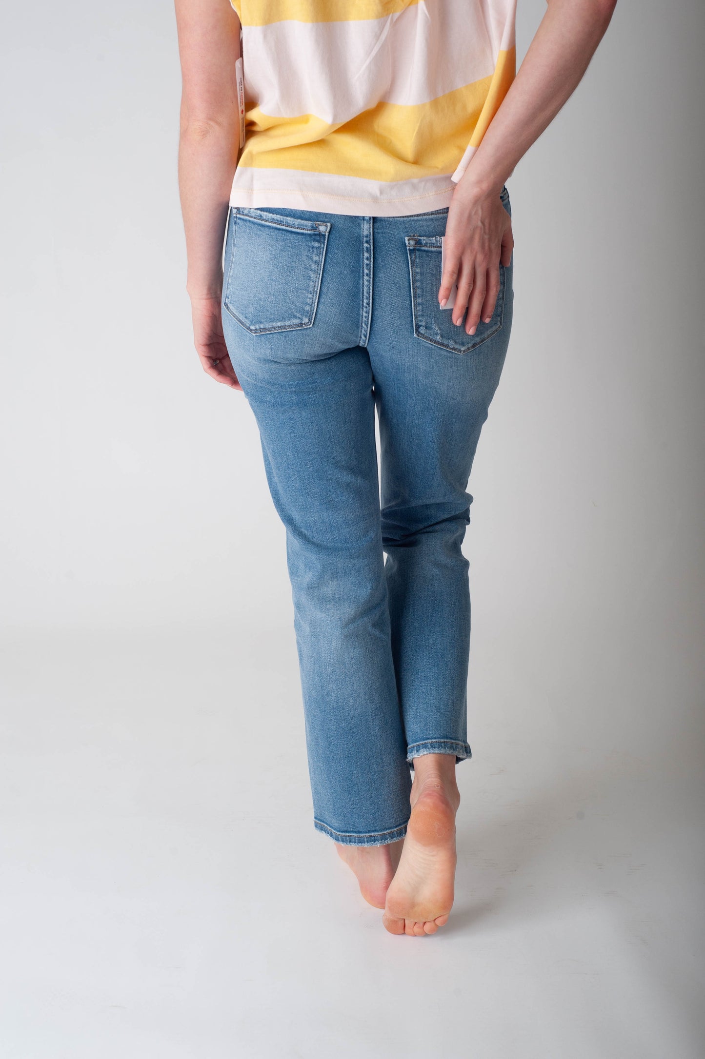 Person wearing blue jeans and a yellow and white striped shirt on a plain background