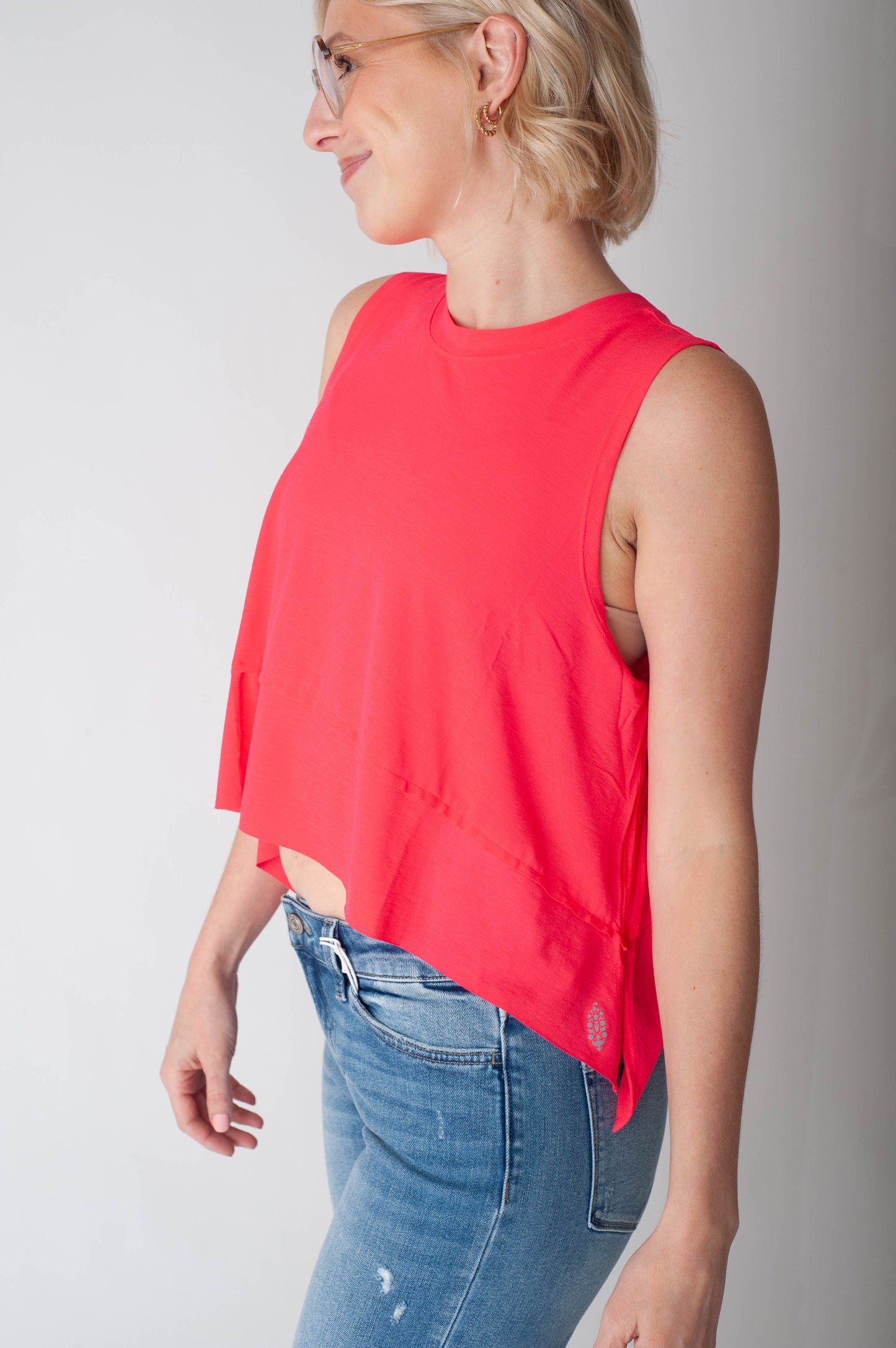 Woman wearing a red sleeveless top and blue jeans against a plain background
