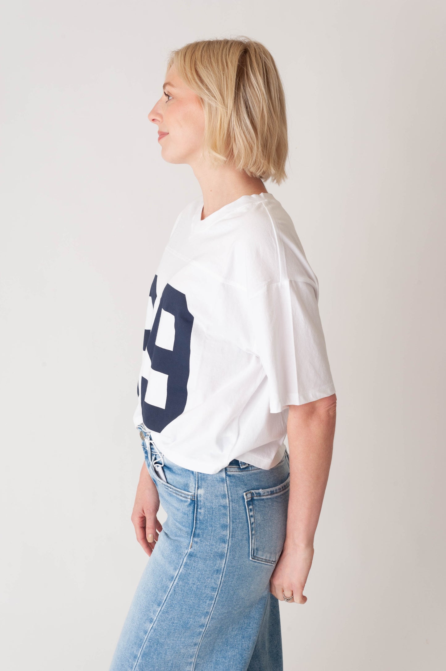 Person wearing a white t-shirt with a blue number 9 on the back, standing against a plain background.