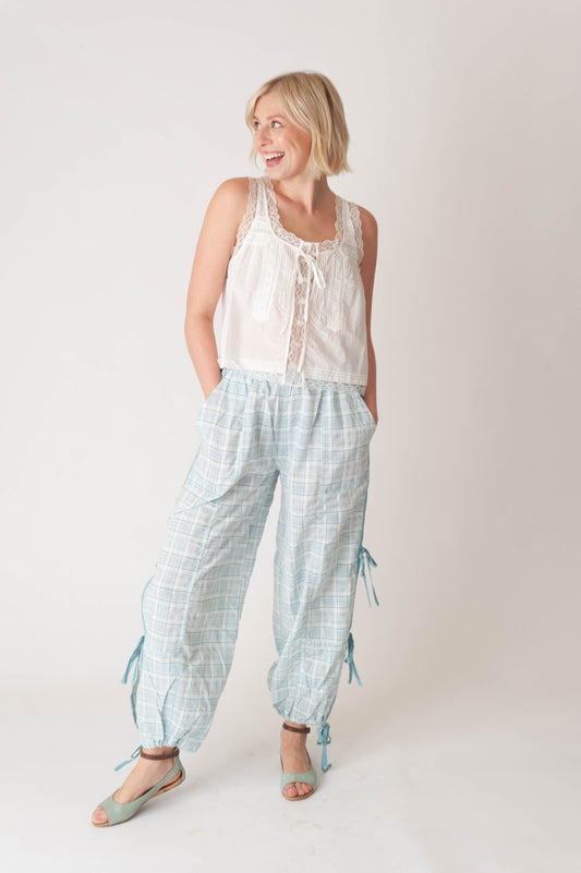 Woman wearing a white sleeveless top and light blue checkered pants on a plain background