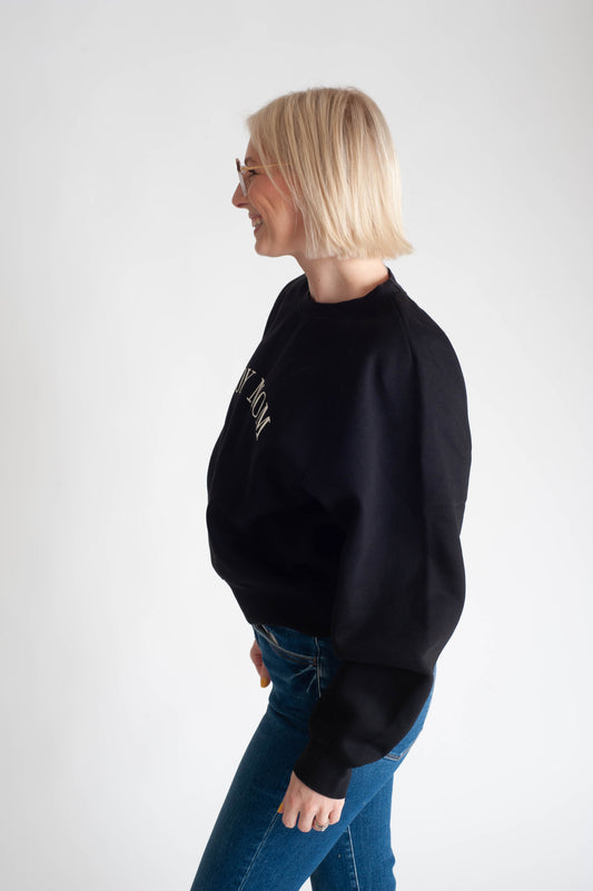 Woman wearing a black sweatshirt and blue jeans on a white background
