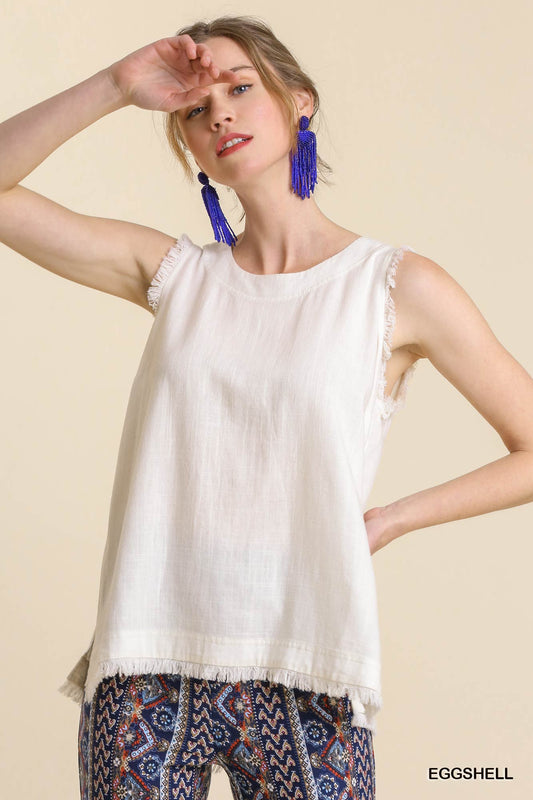 Woman wearing a white sleeveless top with fringe details on a beige background