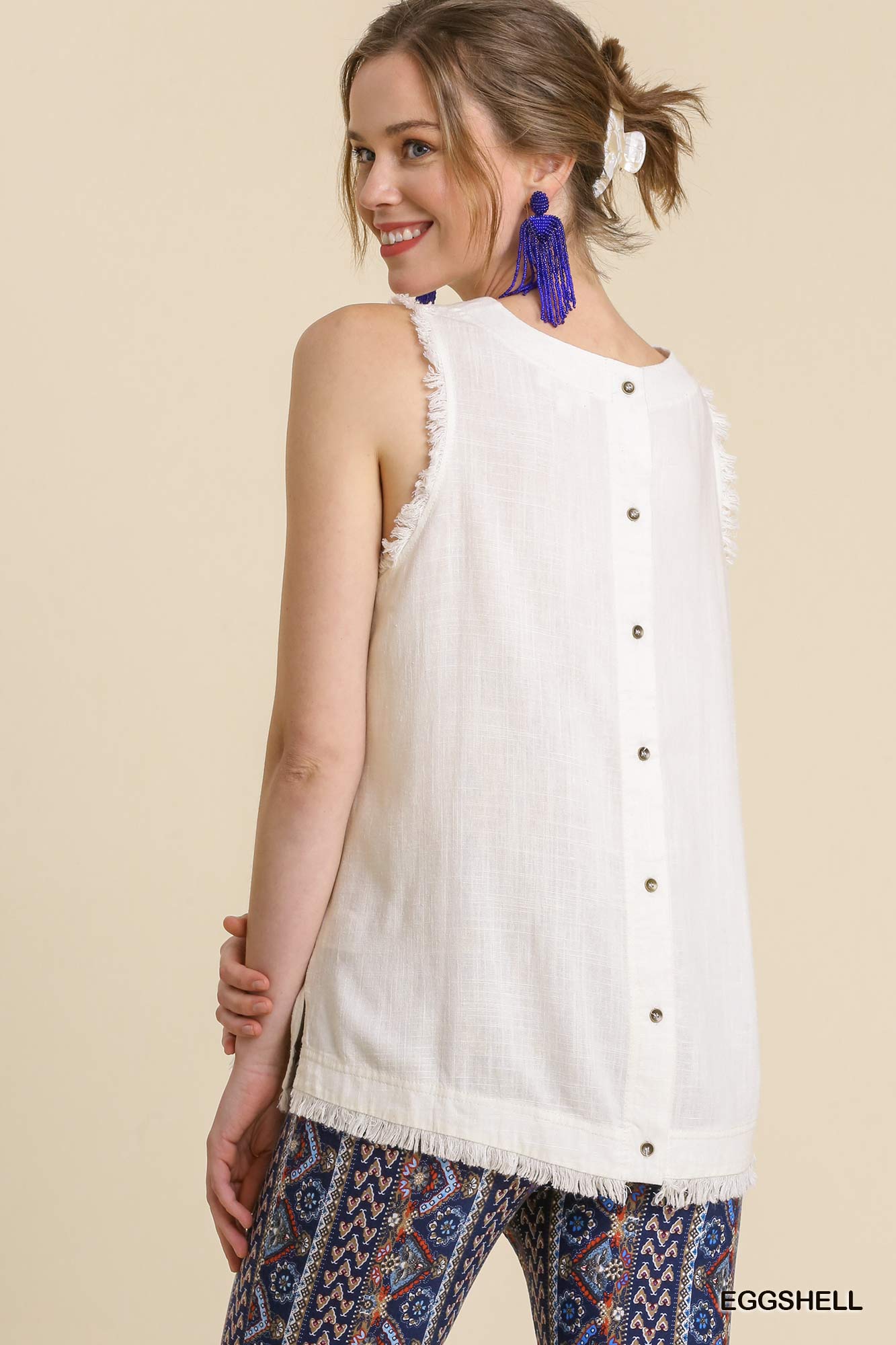 Woman wearing a white sleeveless top with buttons and patterned pants on a beige background