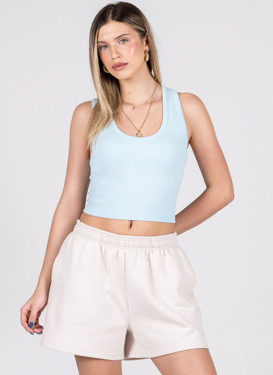 Woman wearing a light blue tank top and beige shorts on a white background