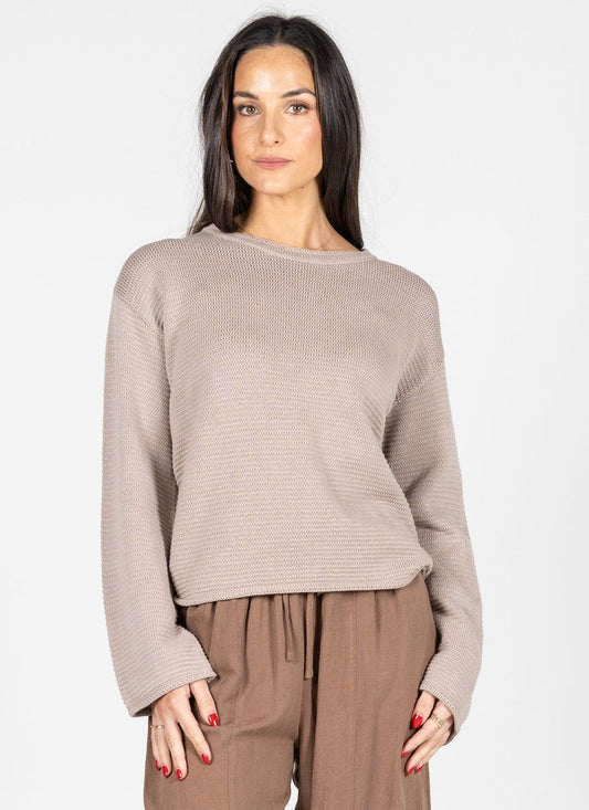Woman wearing a beige sweater and brown pants on a white background