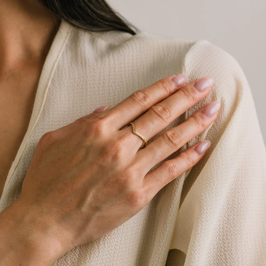 Close-up of a hand wearing a gold ring on beige fabric.