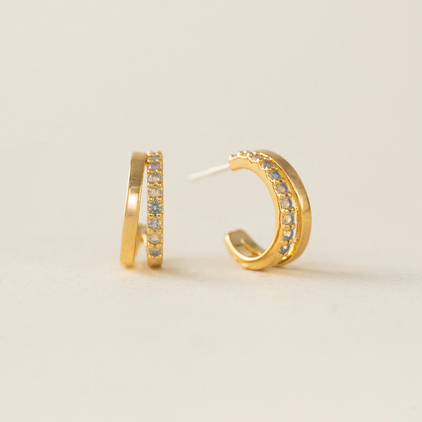 Gold hoop earrings with embedded stones on a light beige background
