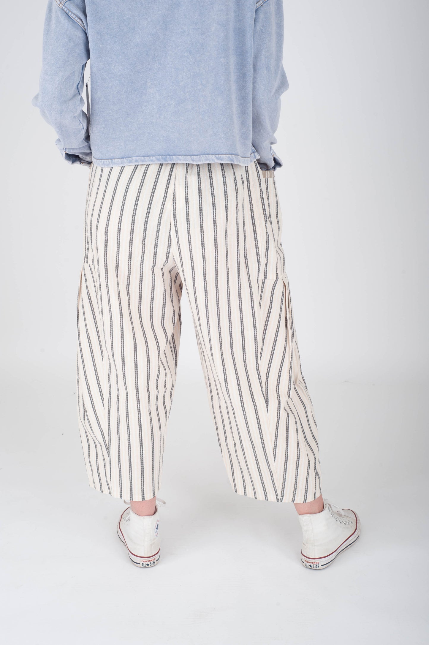 Person wearing light blue sweatshirt and striped pants on a white background
