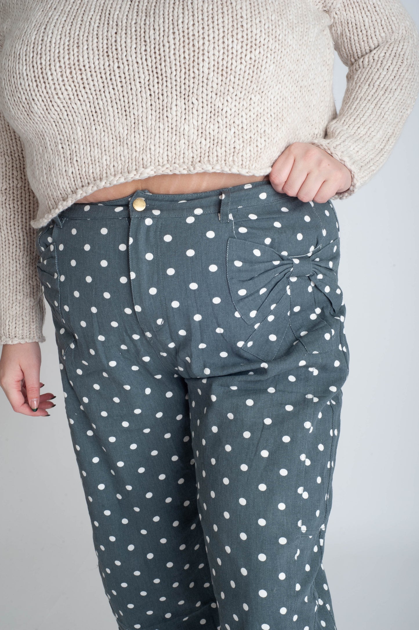 Person wearing a beige sweater and polka dot pants on a plain background