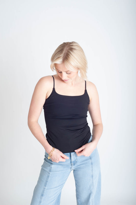 Woman wearing a black tank top and light blue jeans on a white background