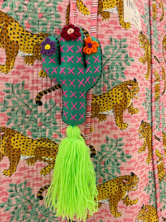 Cactus-shaped bag charm with tassel on a pink fabric background with leopards and plants