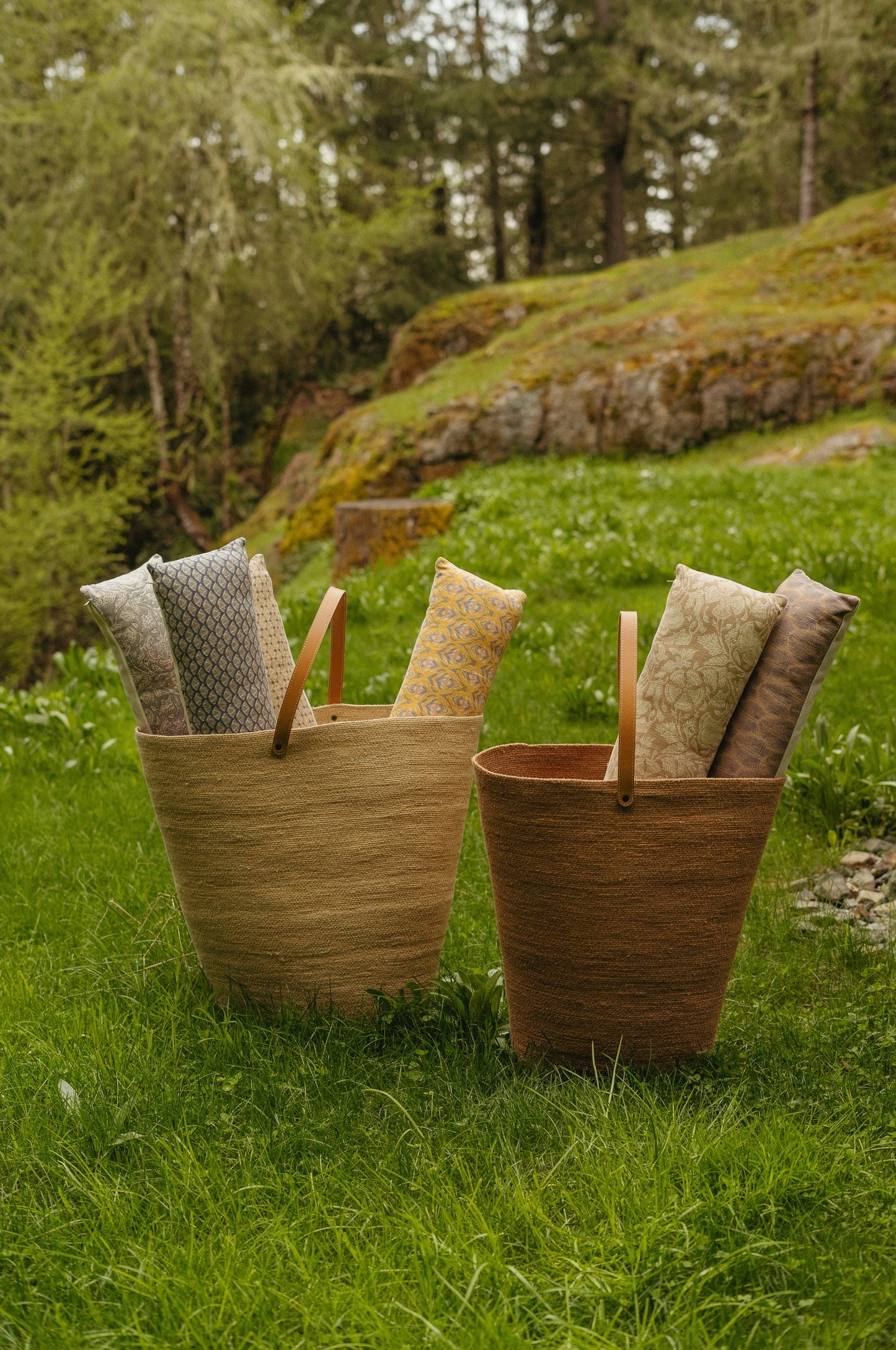 Two woven baskets filled with cushions on a grassy outdoor setting