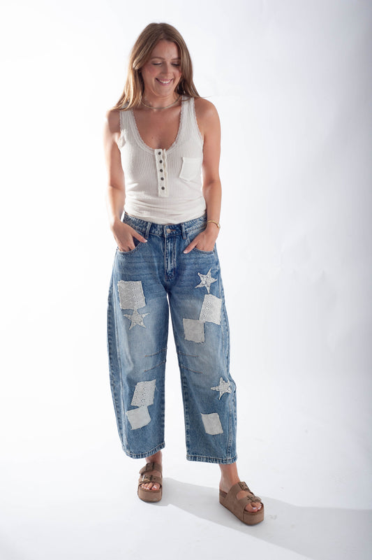 Woman wearing a white tank top and blue jeans with star patterns on a white background
