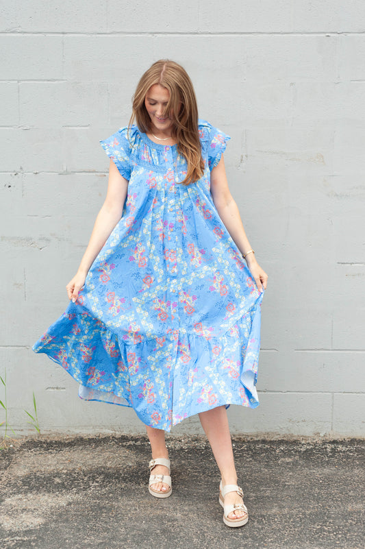 Woman wearing a blue floral dress against a gray wall.