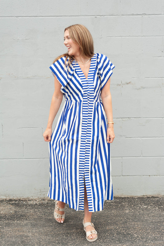 Woman wearing a blue and white striped dress against a gray wall.