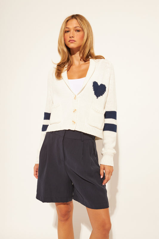 Woman wearing a white cardigan with blue accents and navy shorts on a white background