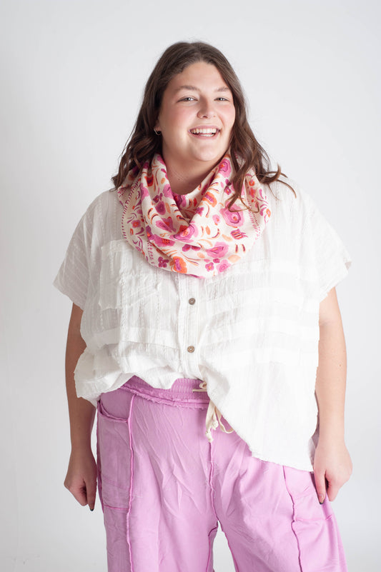 Person wearing a white shirt, pink pants, and a floral scarf on a white background